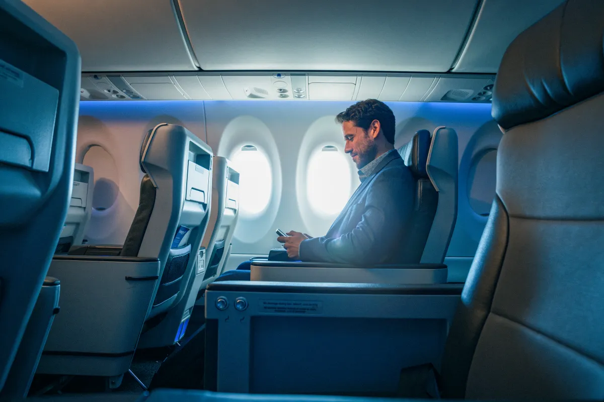 A traveler checking his phone in a cabin lit in soft blue