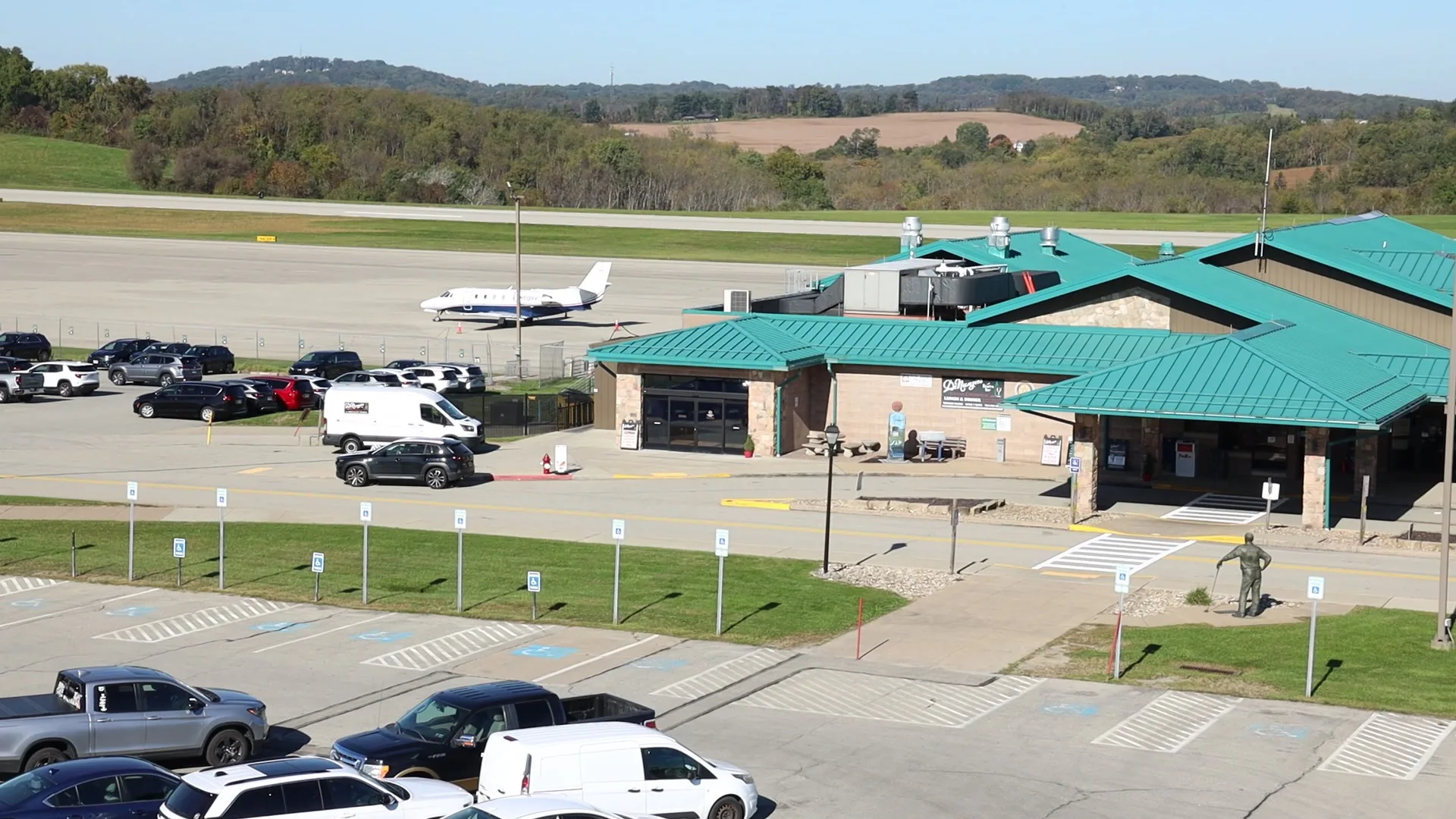The main terminal at Arnold Palmer Regional Airport from the parking lot, with a business jet on the ramp and the ridges behind