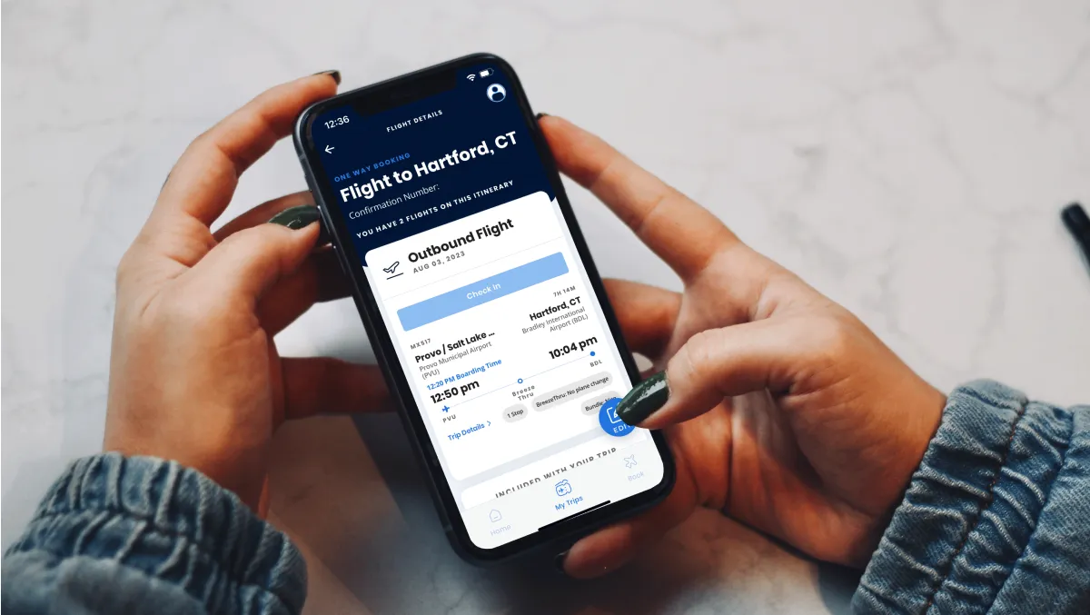 Hands holding a phone with a Breeze Airways flight itinerary on screen