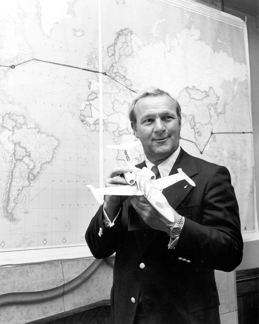 Arnold Palmer holding a model Learjet in front of a world map